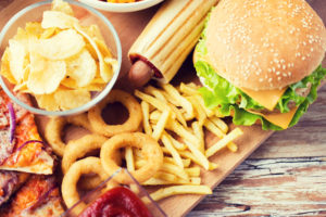 Concetto di fast food e alimentazione malsana - primo piano di hamburger o cheeseburger, anelli di calamari fritti, patatine fritte hotdog e patatine fritte su tavolo di legno vista dall'alto junk food cibi alimenti ultra processati