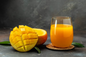 Bicchiere di succo di mango accanto a un mango tagliato a metà
