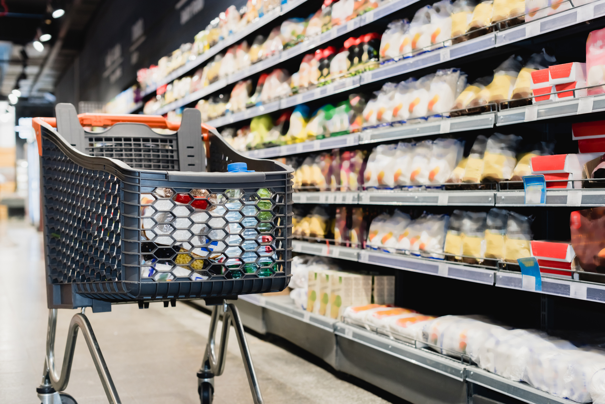 Una carrello pieno nella corsia di un supermercato, davanti a uno scaffale; concept: prezzi