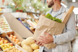 Uomo trasporta tra le braccia una busta di carta con insalata e pane; concept: spesa, supermercato, Rapporto Coop, prezzi