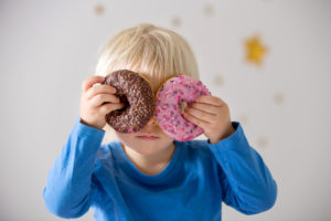 Bambino piccolo tiene due ciambelle o donut davanti agli occhi; concept: ultra processati, junk food, bambini piccoli