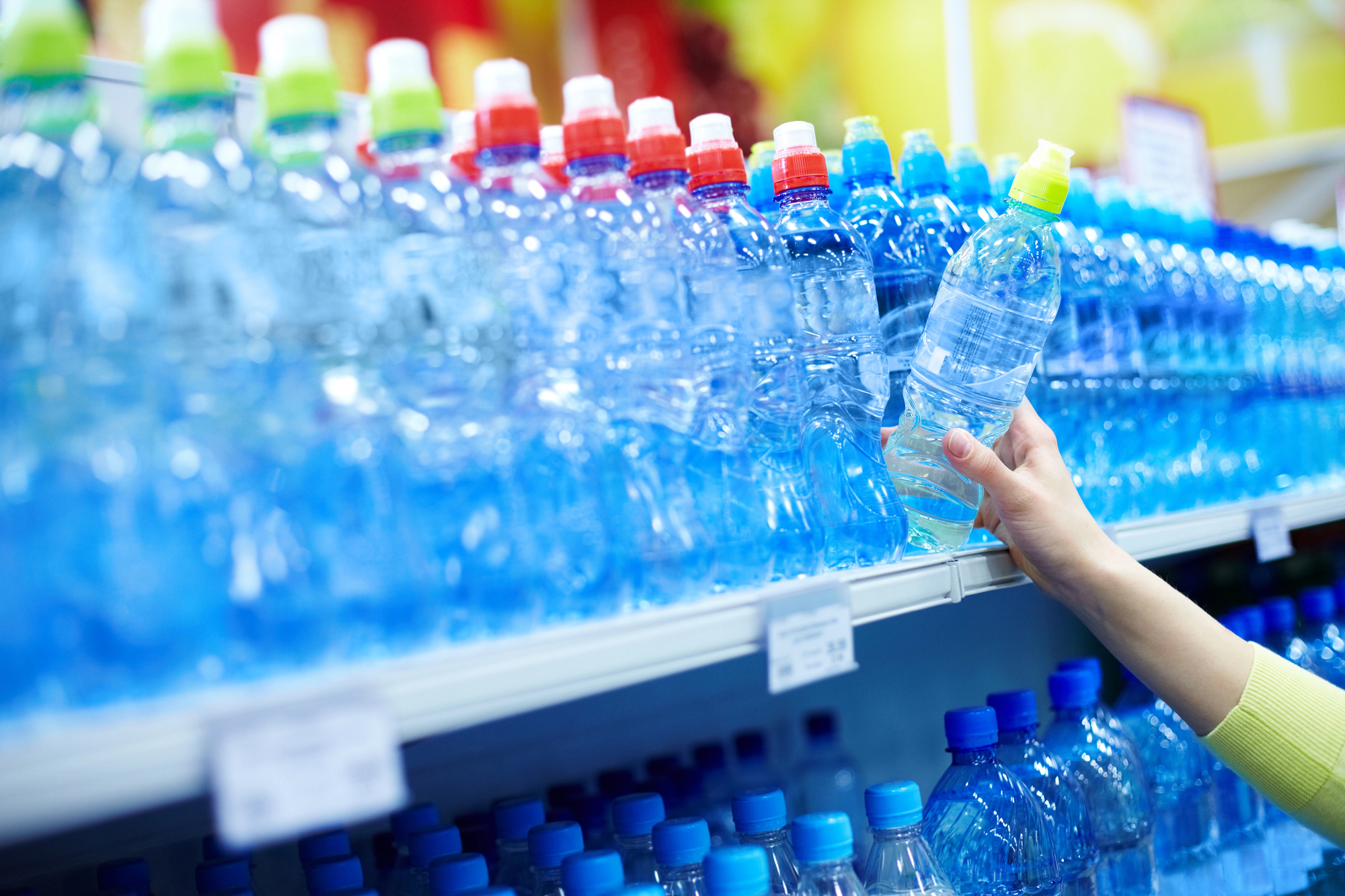 Mano prende una bottiglia di acqua minerale dallo scaffale di un supermercato