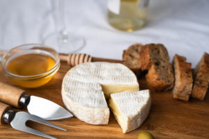 Formaggio a pasta molle tipo brie o camembert su un tagliere di legno con ciotola di miele e fette di pane