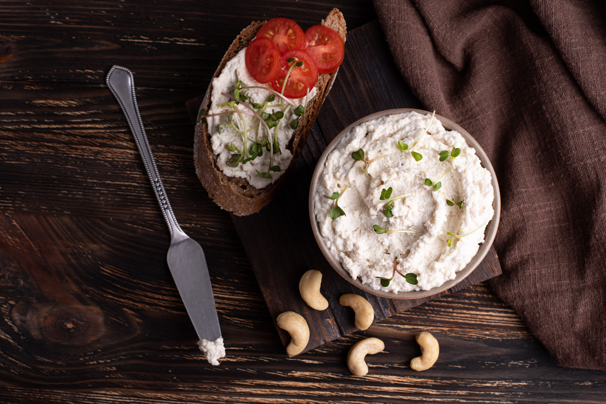 Formaggio vegano fermentato a base di anacardi in una ciotola e su una bruschetta con pomodoro e germogli