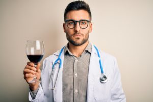 Giovane medico tiene in mano un calice di vino rosso; concept: alcol