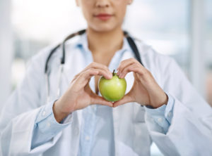 Dottoressa tiene tra le mani a forma di cuore una mela verde; concept: nutrizionista, dietista, medica, medici