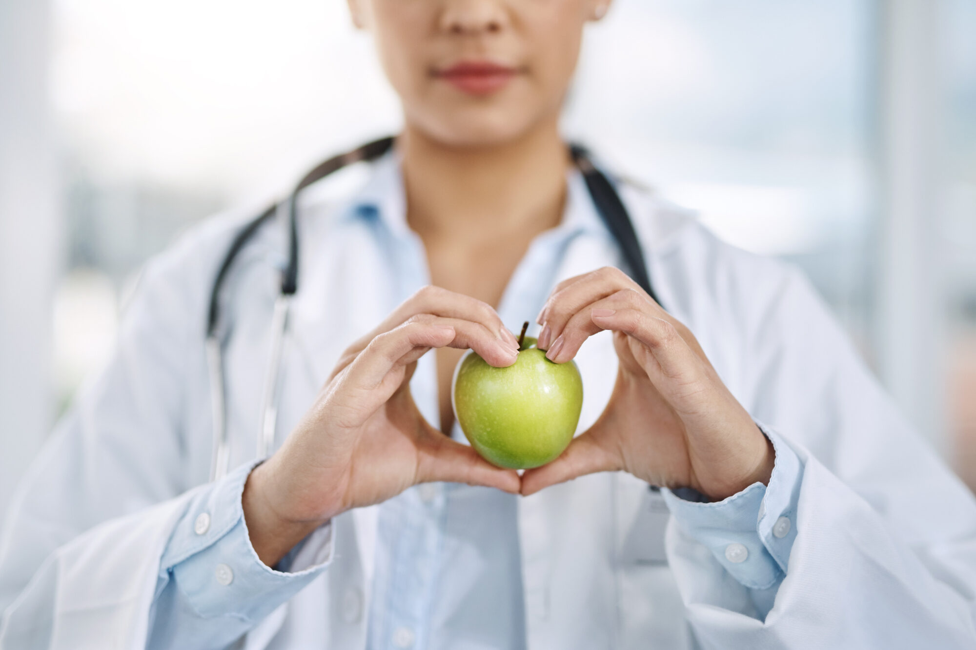 Dottoressa tiene tra le mani a forma di cuore una mela verde; concept: nutrizionista, dietista, medica, medici