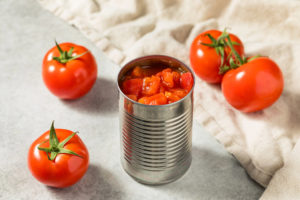 Pomodoro in pezzi in lattina di alluminio, su un tavolo con pomodori interi