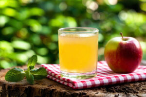 Bicchiere di succo di mela accanto a una mela su una tovaglietta a quadri