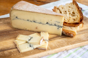 Fetta di formaggio francese Morbier su un tagliere con pezzi di pane e altrefettine di formaggio