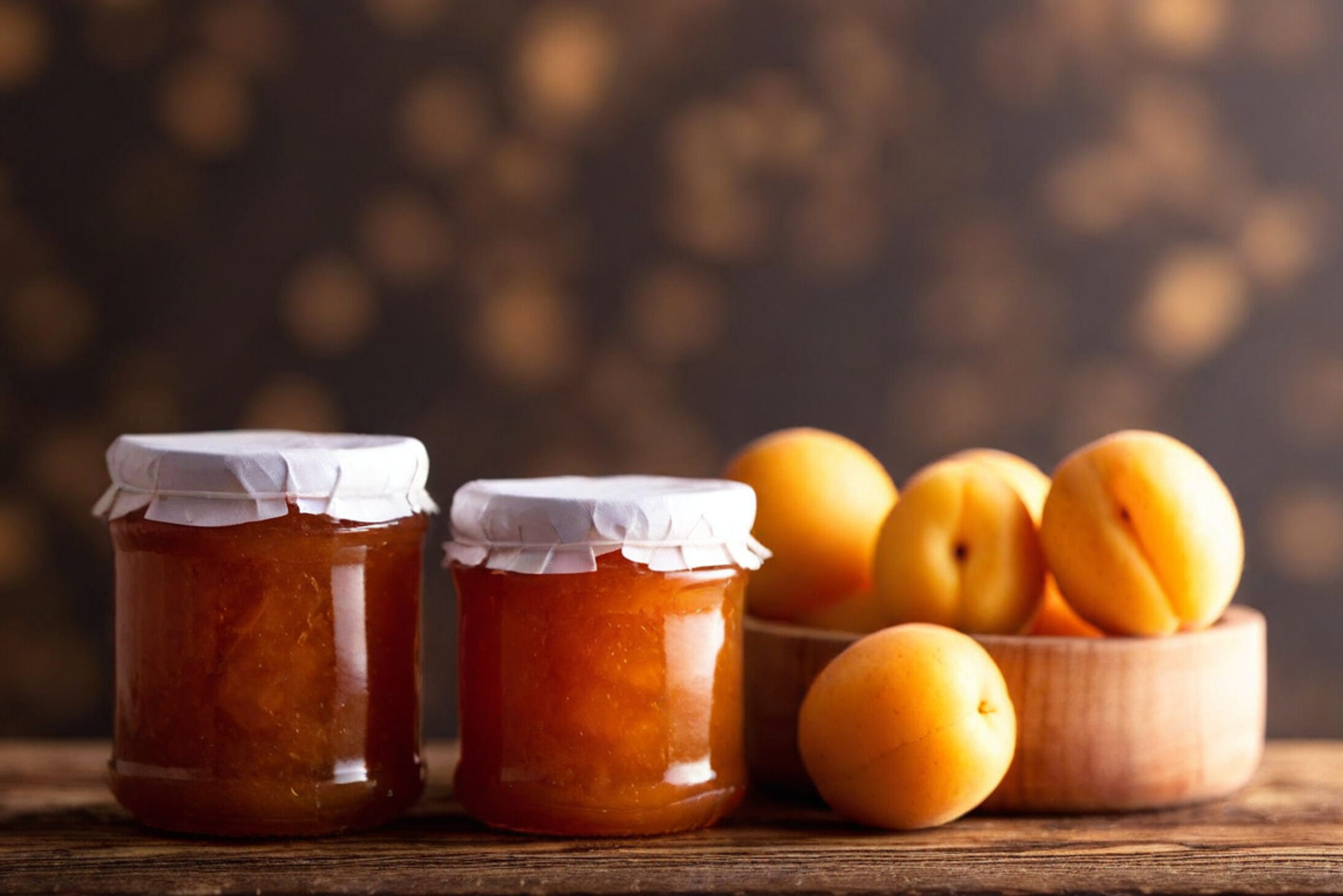 Due vasetti di marmellata di albicocche, accanto ad albicocche sul tavolo; concept: shrinkflation