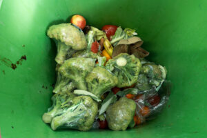 Vista dall'alto di un bidone della spazzatura con broccoli in decomposizione in una confezione di plastica. spreco alimentare