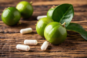 Frutti di Garcinia cambogia accanto a capsule di integratori alimentari su un tavolo; concept: prodotti dimagranti, perdita di peso