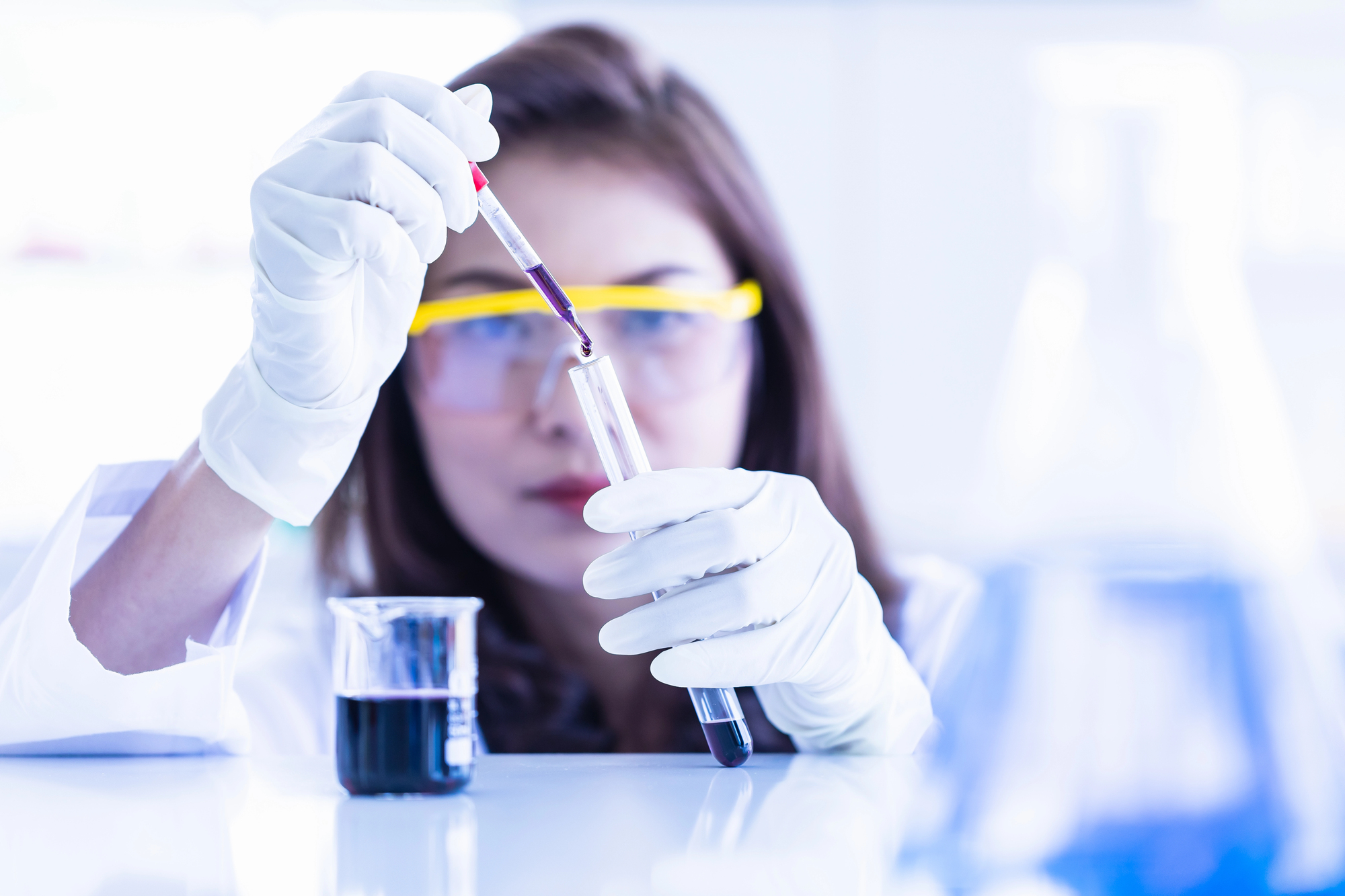 Scienziata o tecnica di laboratorio preleva da una provetta del liquido scuro con una pipetta, sul bancone un becher con altro liquido scuro; concept: cacao, cioccolato, caffè