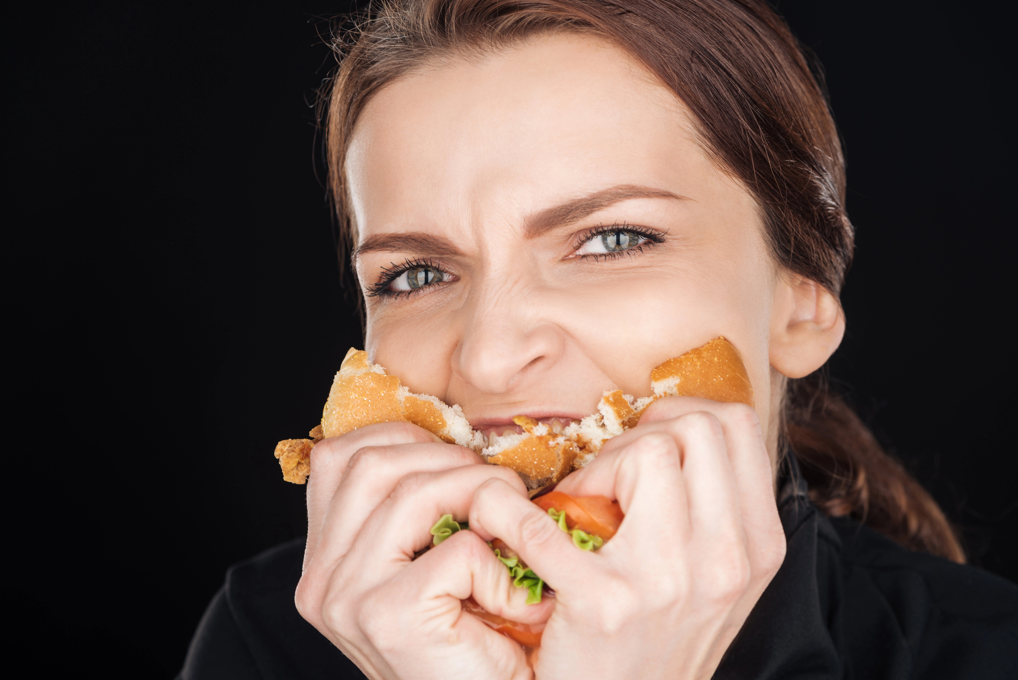 Donna morde un panino con hamburger in maniera aggressiva; concept: fame nervosa, ultra processati, junk food