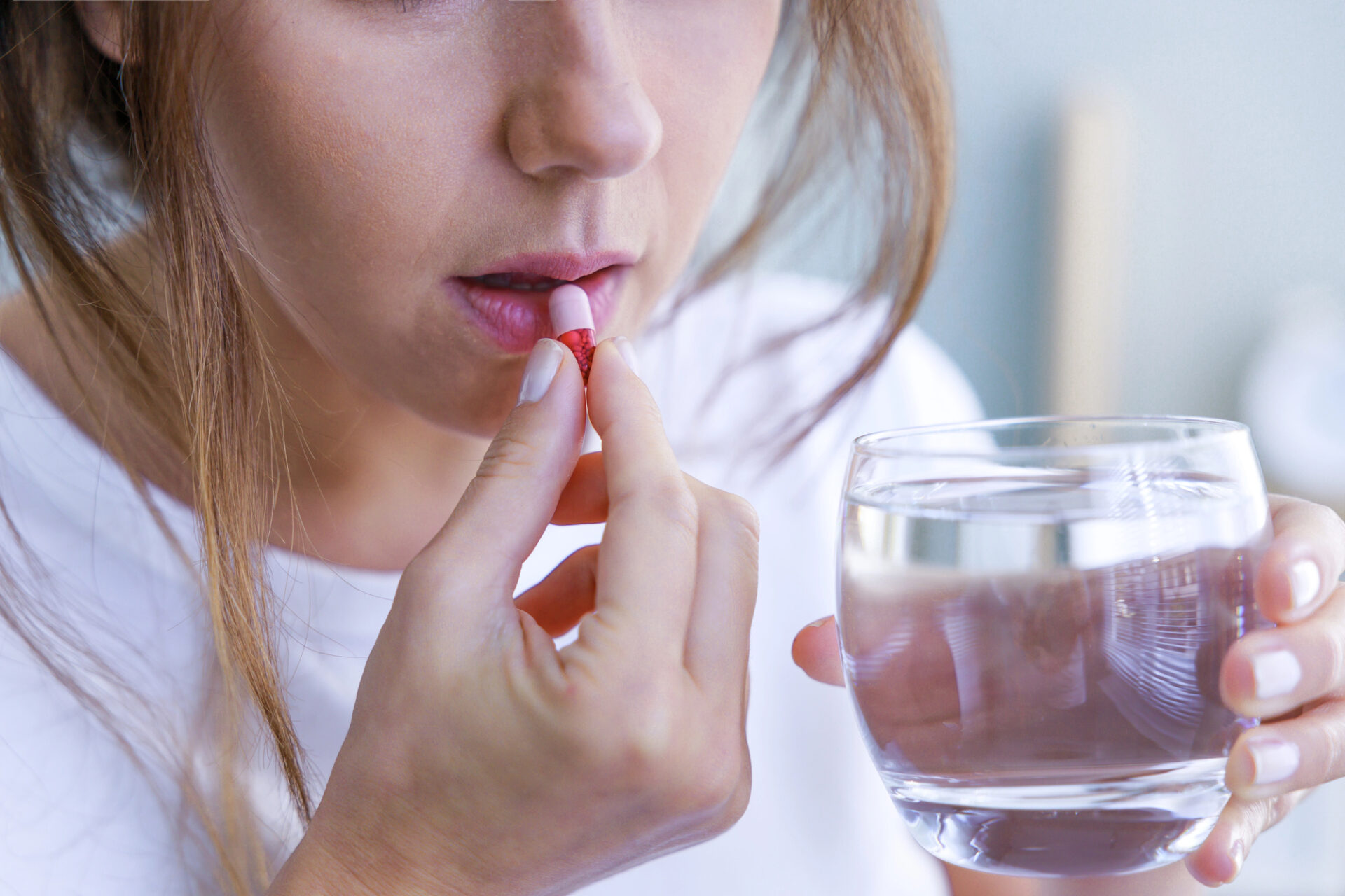Una donna prende una capsula di un farmaco o un integratore con un bicchiere d'acqua; concept: depressione, umore, farmaci, integratori, antibiotici, probiotici, farmaci antivirali