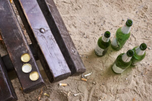 Quattro bottiglie di birra in vetro abbandonate vicino alla panchina di un parco; concept: rifiuti, vuoto a rendreå