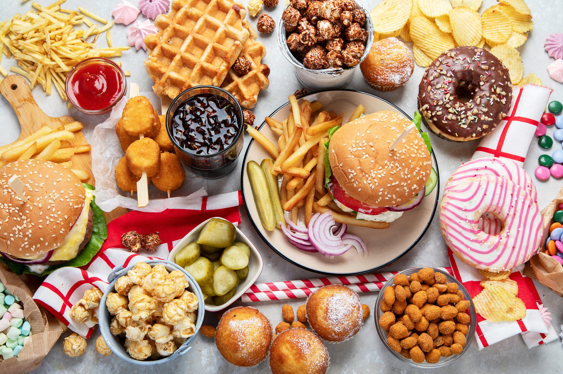 Assortimento di cibo spazzatura visto dall'alto: panini con hamburger, nuggets, pop corn, patatine, waffle, donut glassati, cupcake, marshmallow, ketchup; concept: snack, junk food, ultra processati