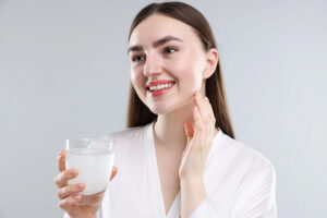 Giovane donna sorridente tiene in mano un bicchiere con integratore di collagene ; concept: pelle, invecchiamento, integratori