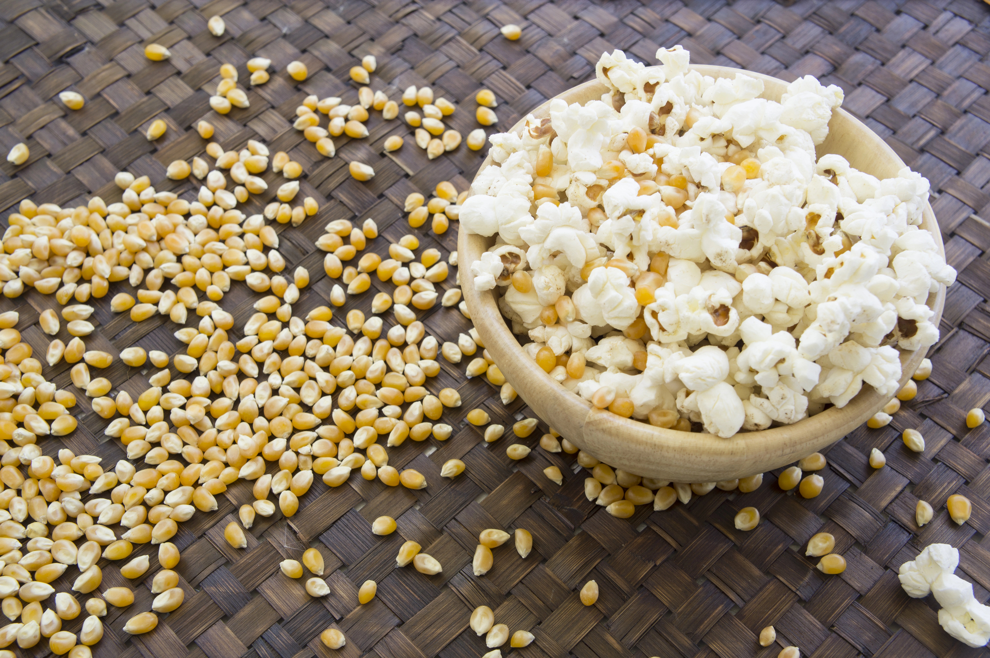 Una ciotola di pop corn, con accanto chicchi di mais ancora crudi sparsi su un tavolo
