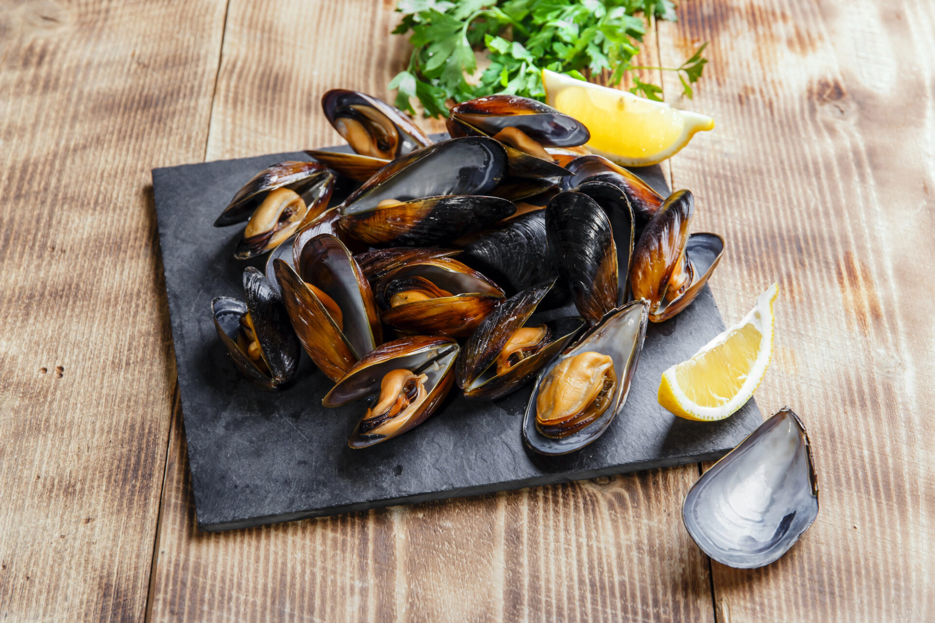 Cozze o mitili su vassoio di ardesia con limone e prezzemolo; concept: molluschi, frutti di mare