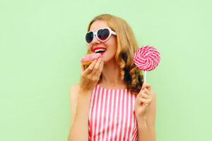 donut junk food dessert dolci zuccheri zucchero ragazza che mangia una ciambella mentre tiene in mano un lecca-lecca su uno sfondo verde