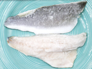 Due filetti di branzino surgelati su un piatto azzurro; concept: pesce surgelato, congelato