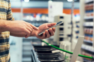 Un uomo digita qualcosa sullo smartphone, dentro un supermercato