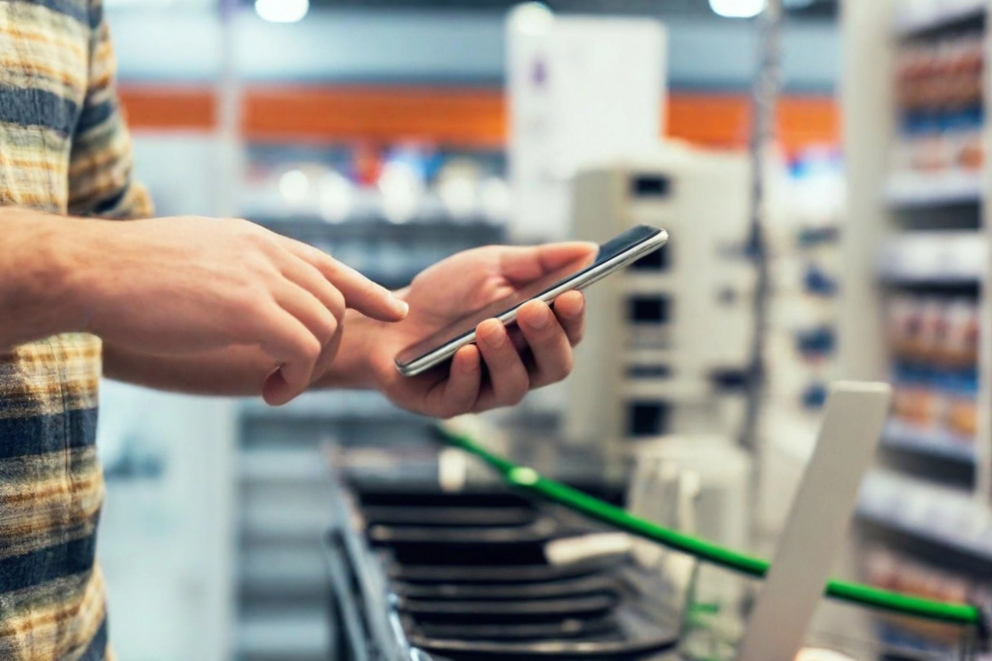 Un uomo digita qualcosa sullo smartphone, dentro un supermercato