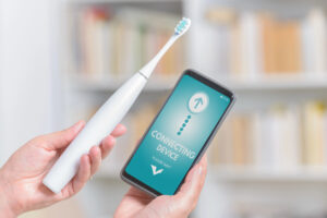 Una persona tiene in una mano uno spazzolino elettrico connesso e nell'altra uno smartphone con un'app aperta su una schermata di connessione