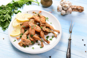 Piatto di cosce di rana con fette di limone, attorno erbe aromatiche e teste d'aglio; concept: rane