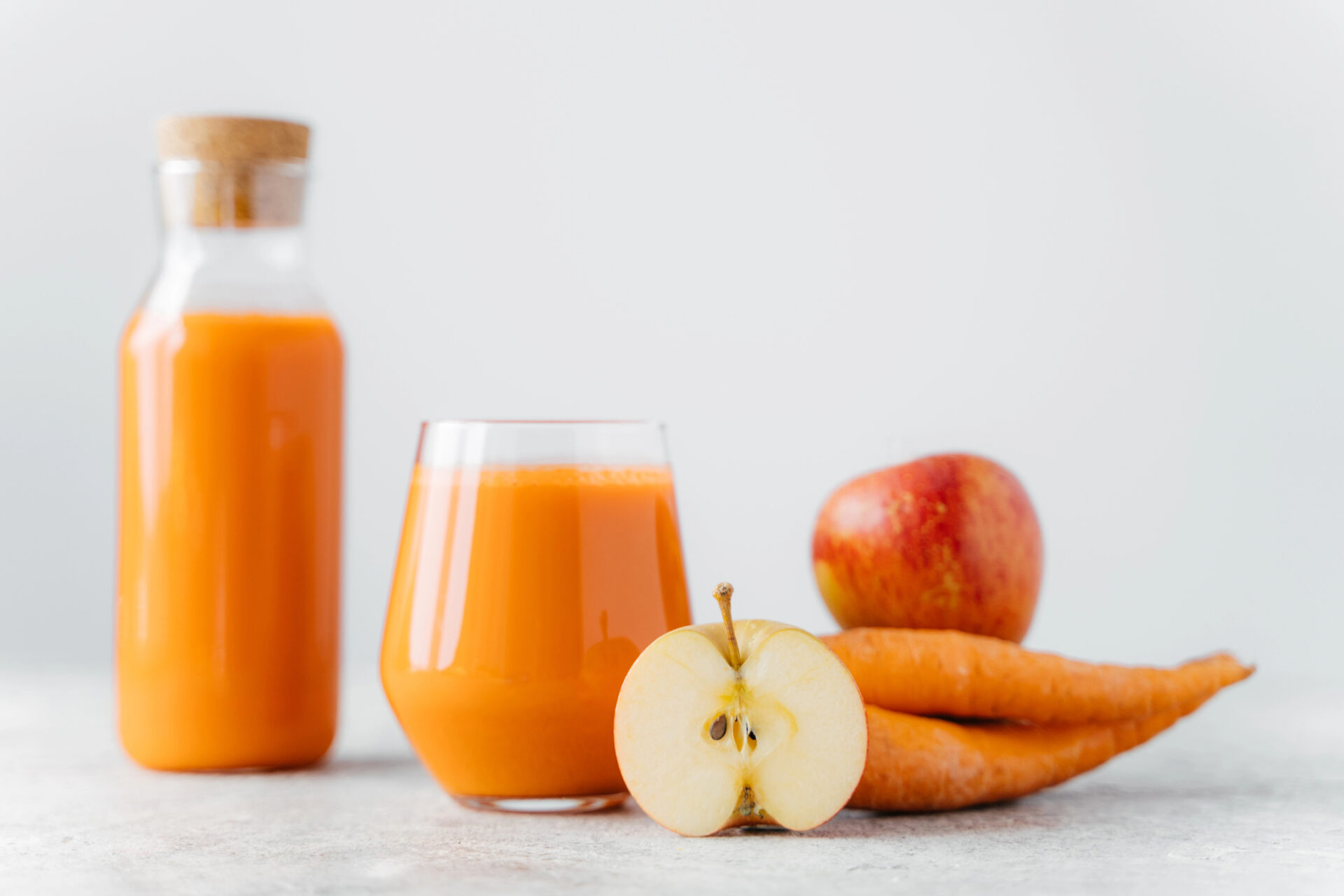 Una bottiglia e un bicchiere di succo di mela e carota, accanto a una mela intera, mezza mela e carote