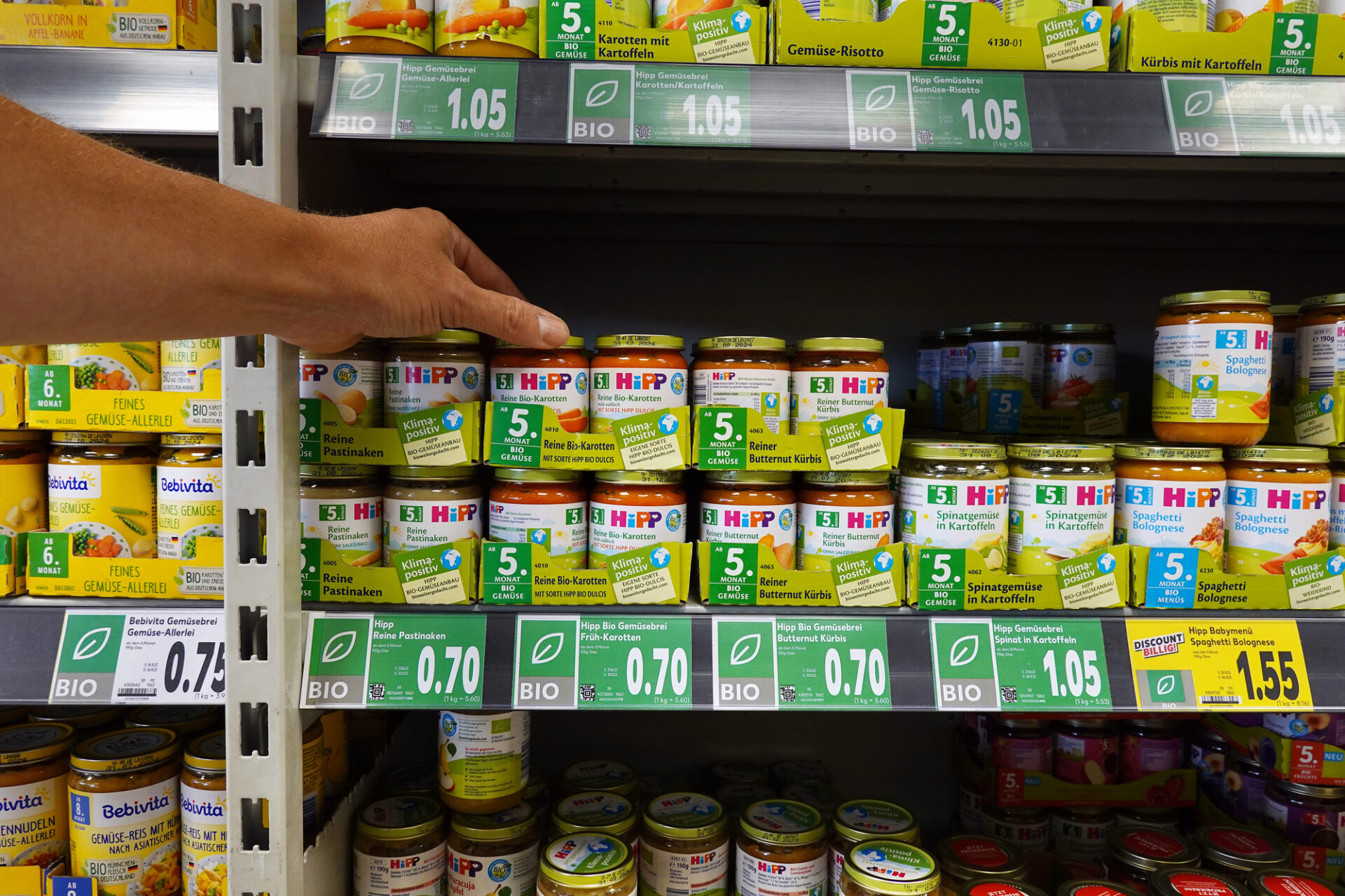 Una persona preleva un vasetto di omogeneizzato HiPP dallo scaffale di un supermercato o negozio specializzato; concept: baby food