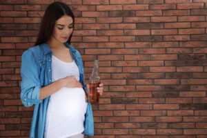 Una giovane donna incinta con in mano una bottiglia di bibita o birra analcolica