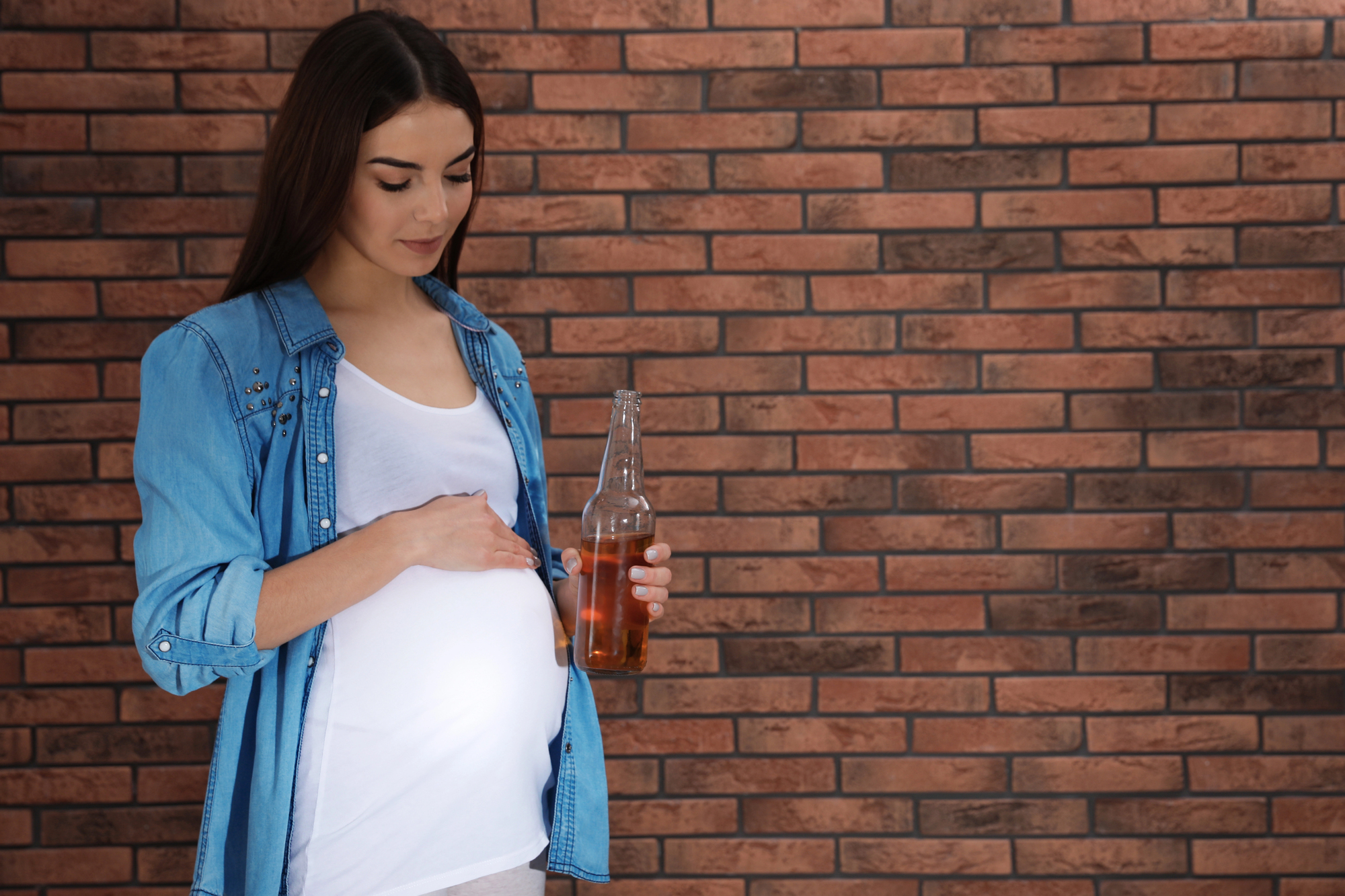 Una giovane donna incinta con in mano una bottiglia di bibita o birra analcolica