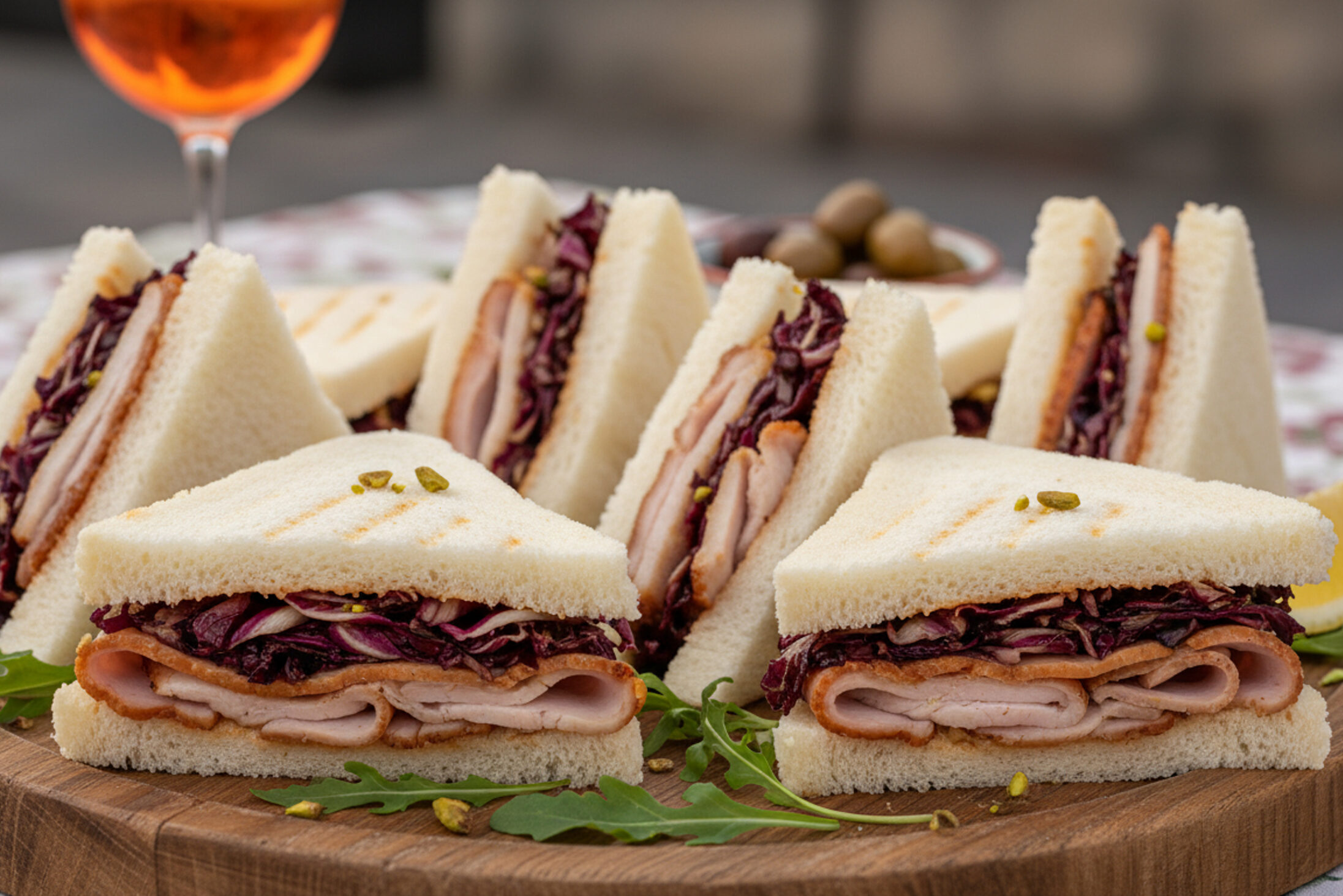 Un piatto di legno con tramezzini vicentini radicchio e porchetta; sullo sfondo un bicchiere di spritz