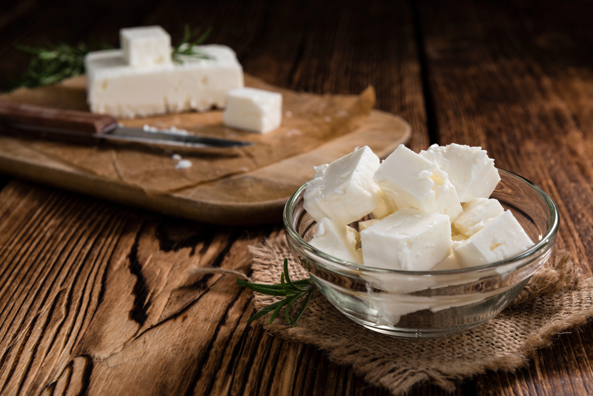 Una ciotola di feta a cubetti, sullo sfondo tagliere con un blocco di feta e un coltello; concept: formaggi dop, latticini