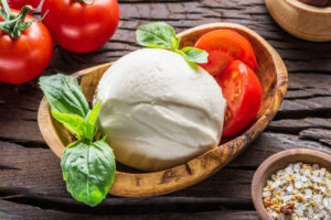 Una mozzarella di bufala o vaccina in una ciotola di legno con pomodori e basilico, intorno altri pomodori e una ciotola di sale misto ad aglio granulare ed erbe aromatiche