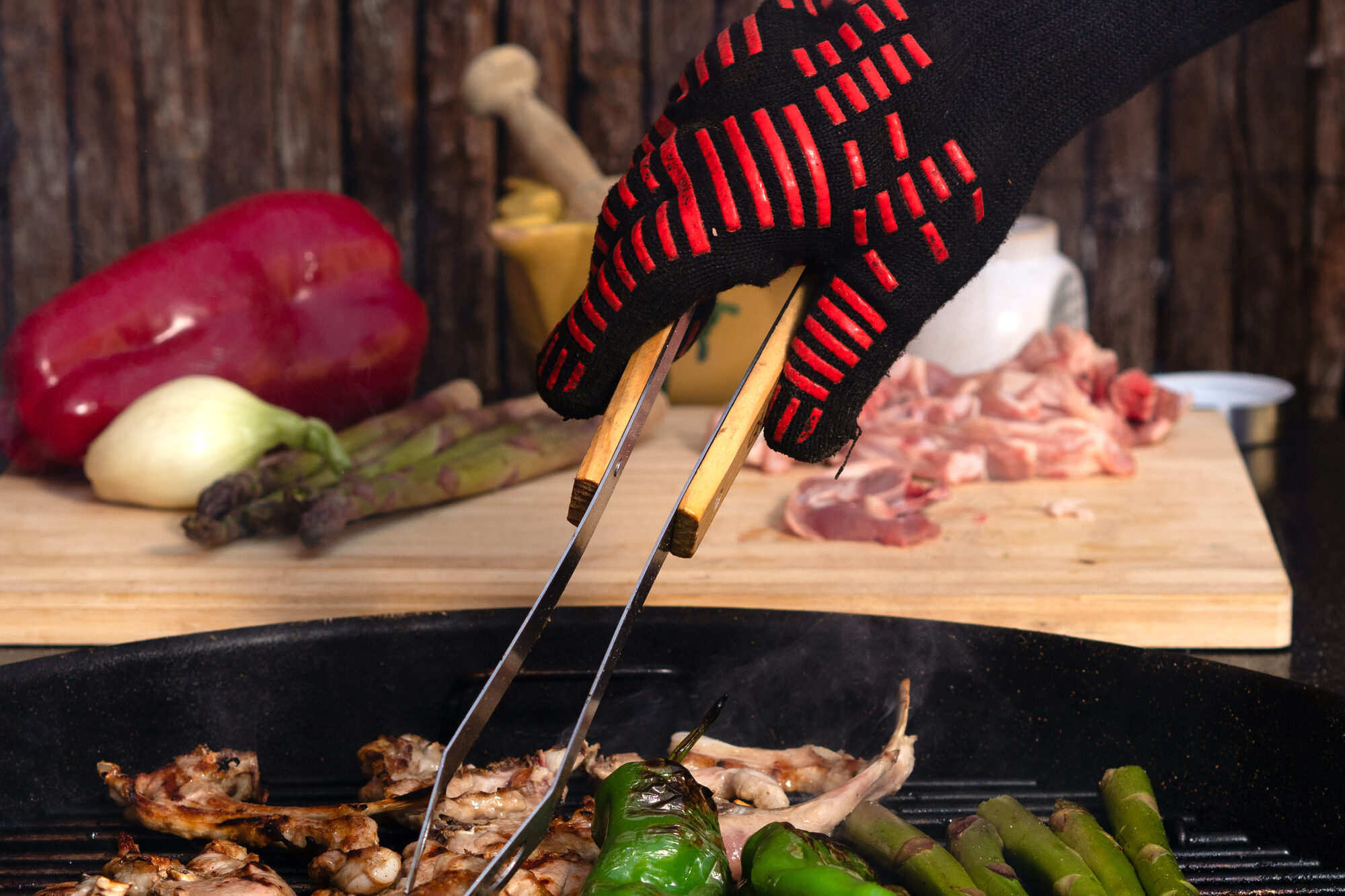 Una persona con guanto protettivo gira carne e verdure su un barbecue