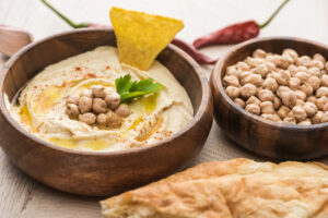 Ciotola di hummus di ceci con ceci, olio extravergine, sesamo, coriandolo e una nacho chip, accanto a una ciotola di ceci secchi e fette di pane tipo pita