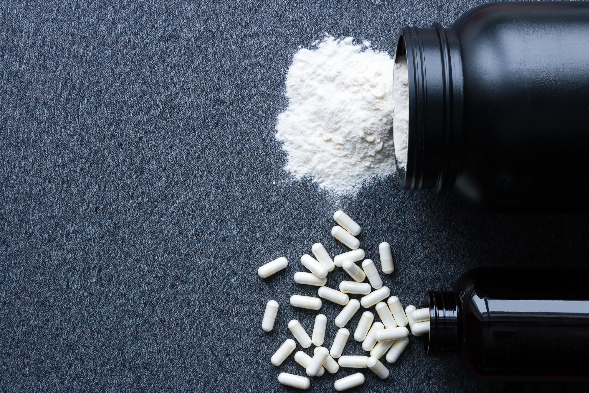 Un barattolo rovesciato di proteine o creatina, accanto a un barattolo rovesciato di integratori alimentari; concept: palestra, bodybuilding