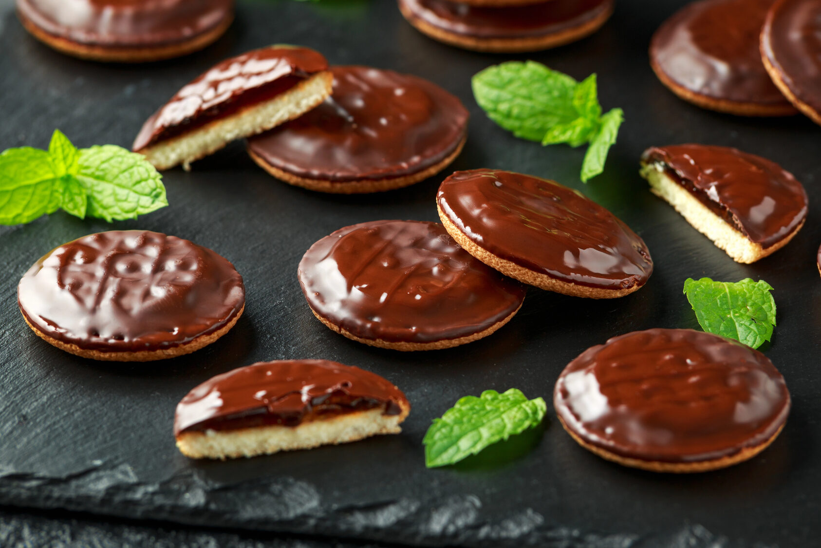 Biscotti tipo jaffa cake su un piatto di ardesia con foglioline di menta; concept: dolci