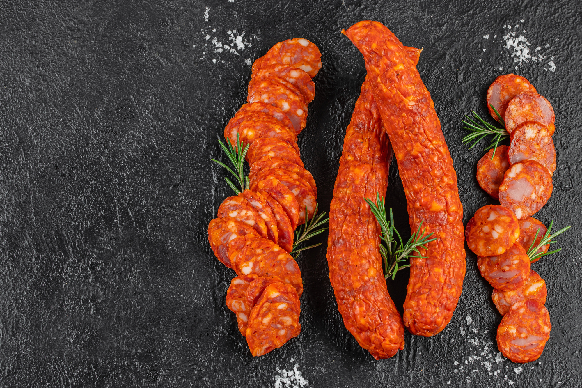 Quattro salami o salsicce piccanti, due intere al centro e due a fette; concept: salame, salumi