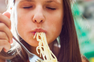 Bambina o adolescente mangia una forchettata di spaghetti; concept: carboidrati