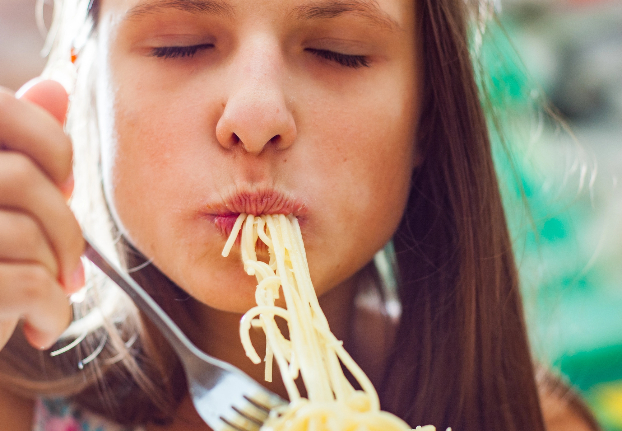 Bambina o adolescente mangia una forchettata di spaghetti; concept: carboidrati