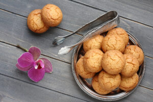 Un ciotola di metallo piena di amaretti, accanto a una pinza, un fiore di orchidea e due amaretti isolati