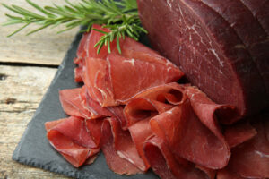 Fette di bresaola acconto a un pezzo di bresaola intero, su un piatto di ardesia con un rametto di rosmarino