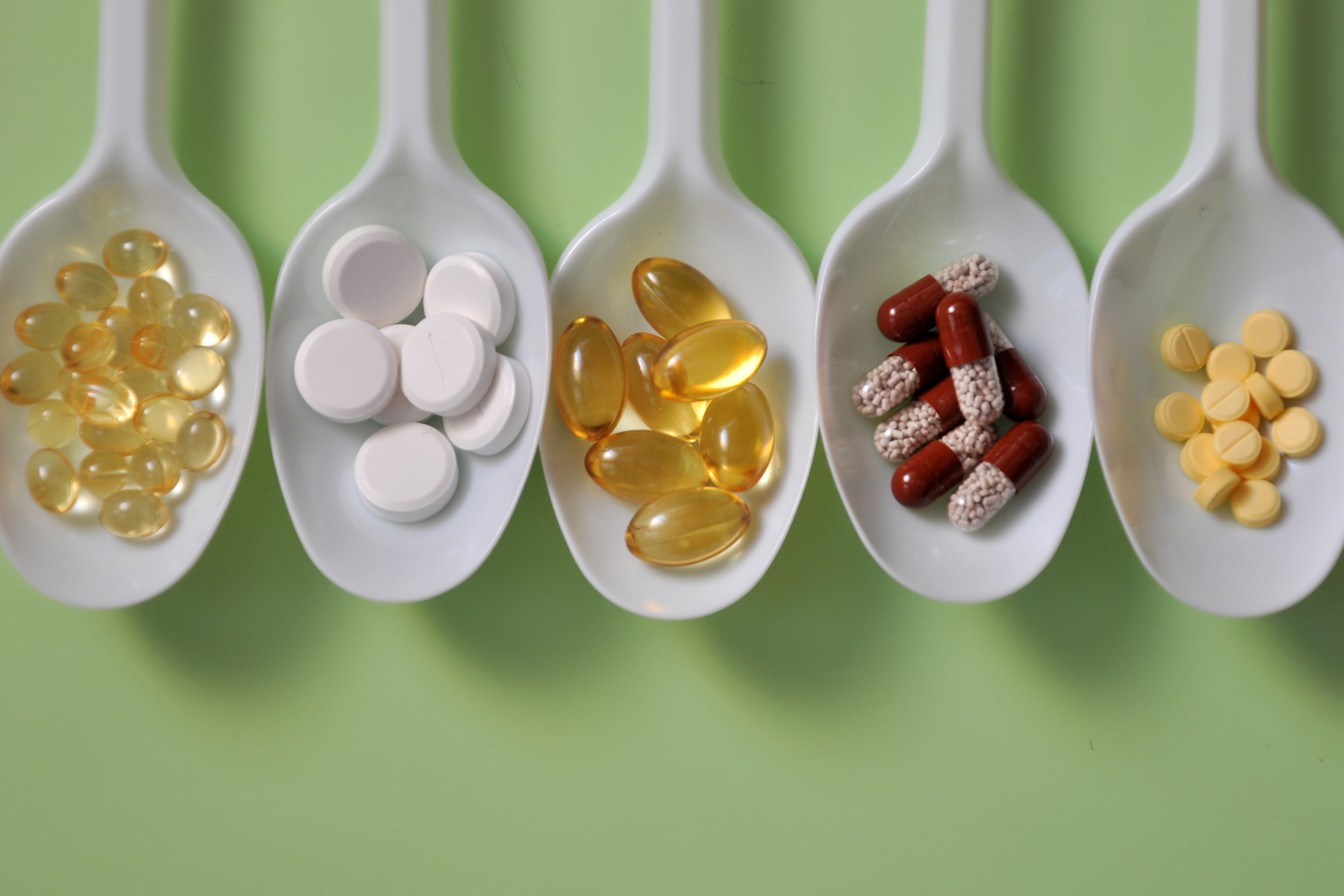 Compresse, capsule, integratori alimentari, vitamine su cucchiaini bianchi. Sfondo medico con pillole