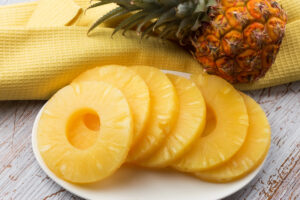 Ananas a fette su un piattino, sullo sfondo un ciuffo d'ananas su un canovaccio giallo