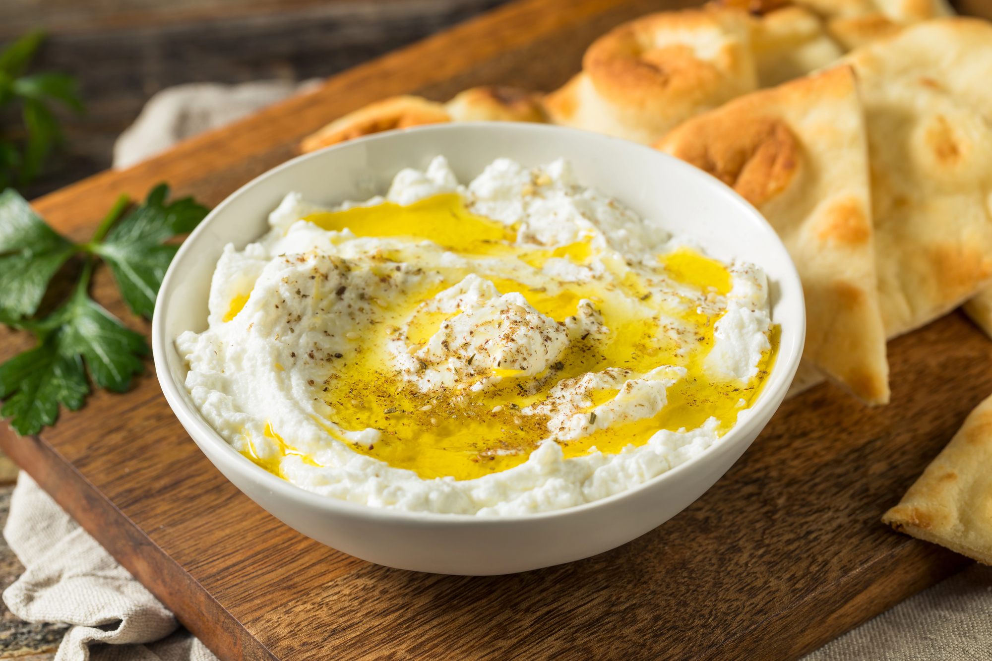 Formaggio fresco labneh con olio d'oliva extravergine su un tagliere di legno, pane tipo pita o focaccia sullo sfondo